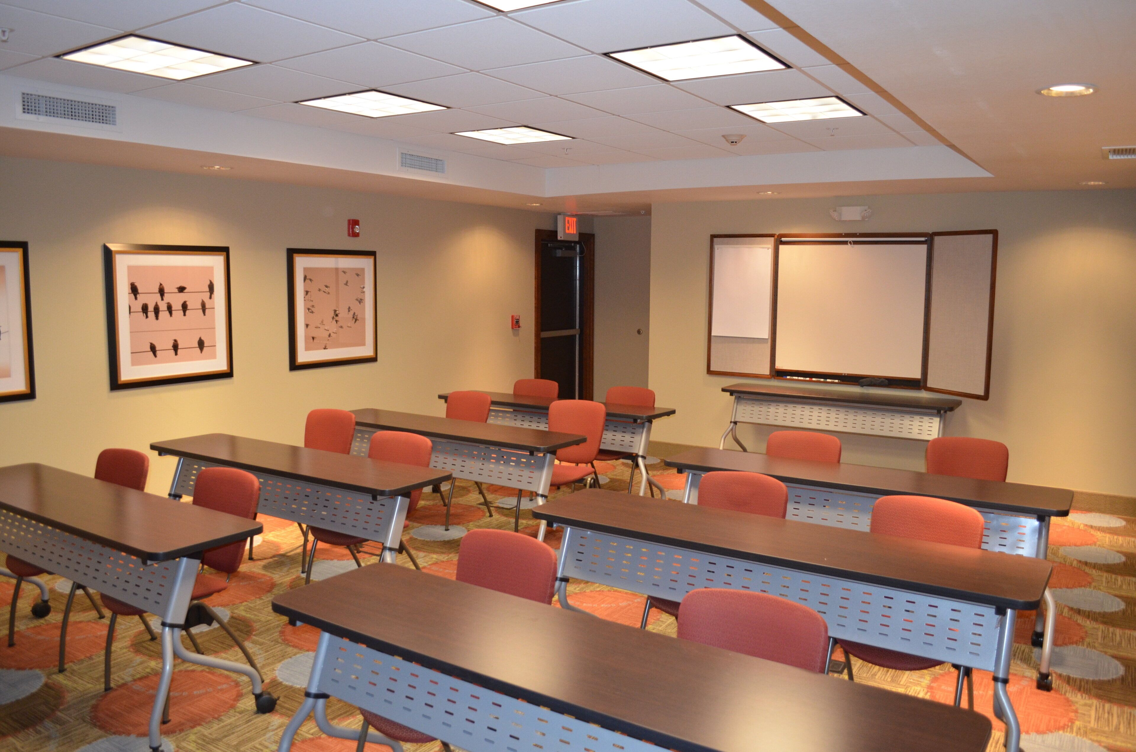 A conference room with multiple tables and chairs, a whiteboard, and framed pictures on the walls.