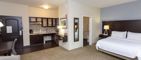 A hotel room with a bed, a desk, a chair, a kitchenette, and a bathroom.