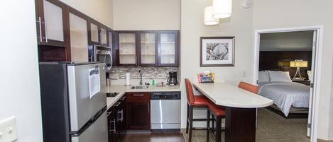 Una cocina compacta equipada con refrigerador, estufa, lavavajillas y un comedor con mesa y sillas.