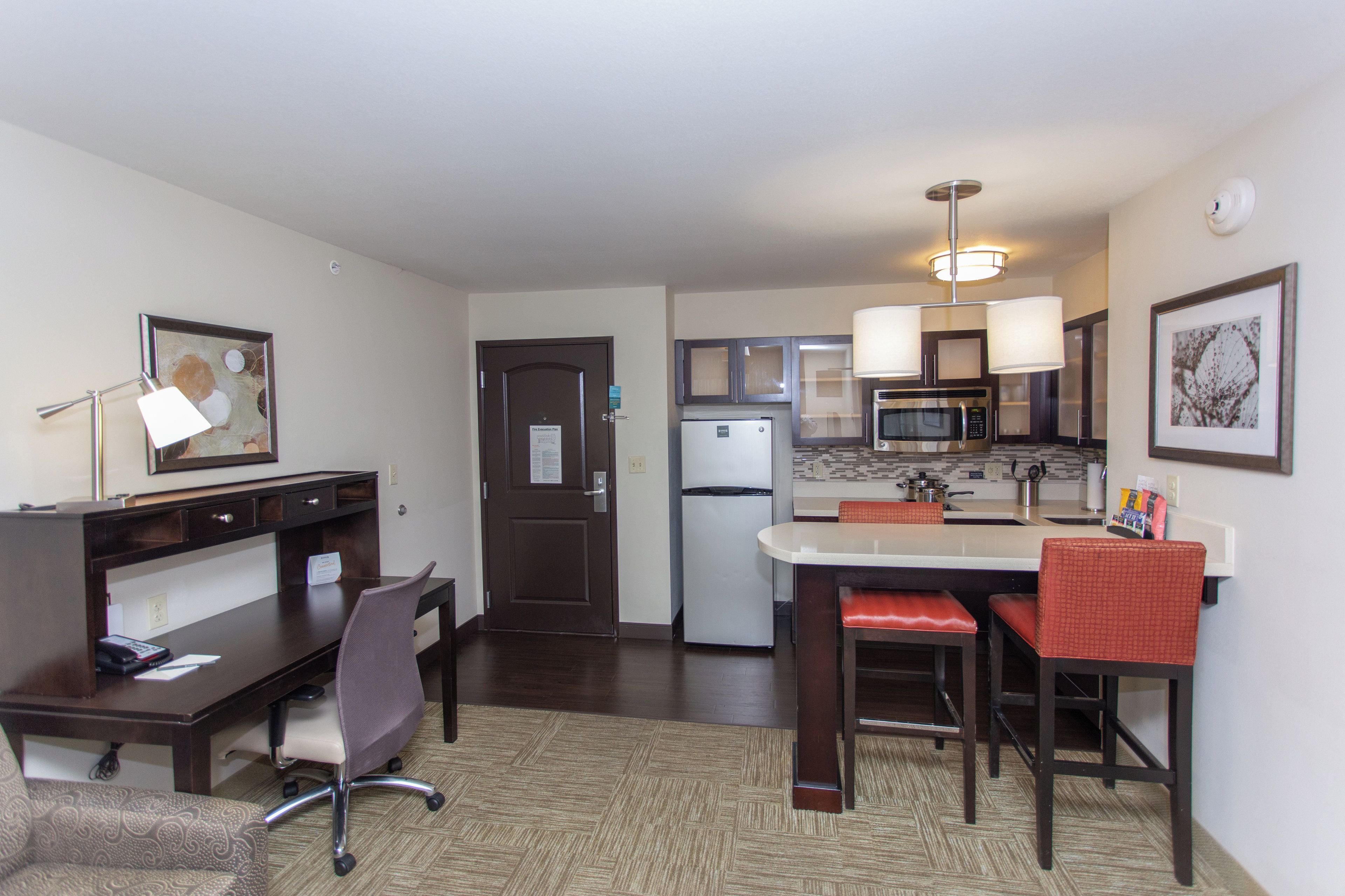 A compact hotel room with a kitchenette, a dining area with a table and chairs, a desk with a chair, and a bed.