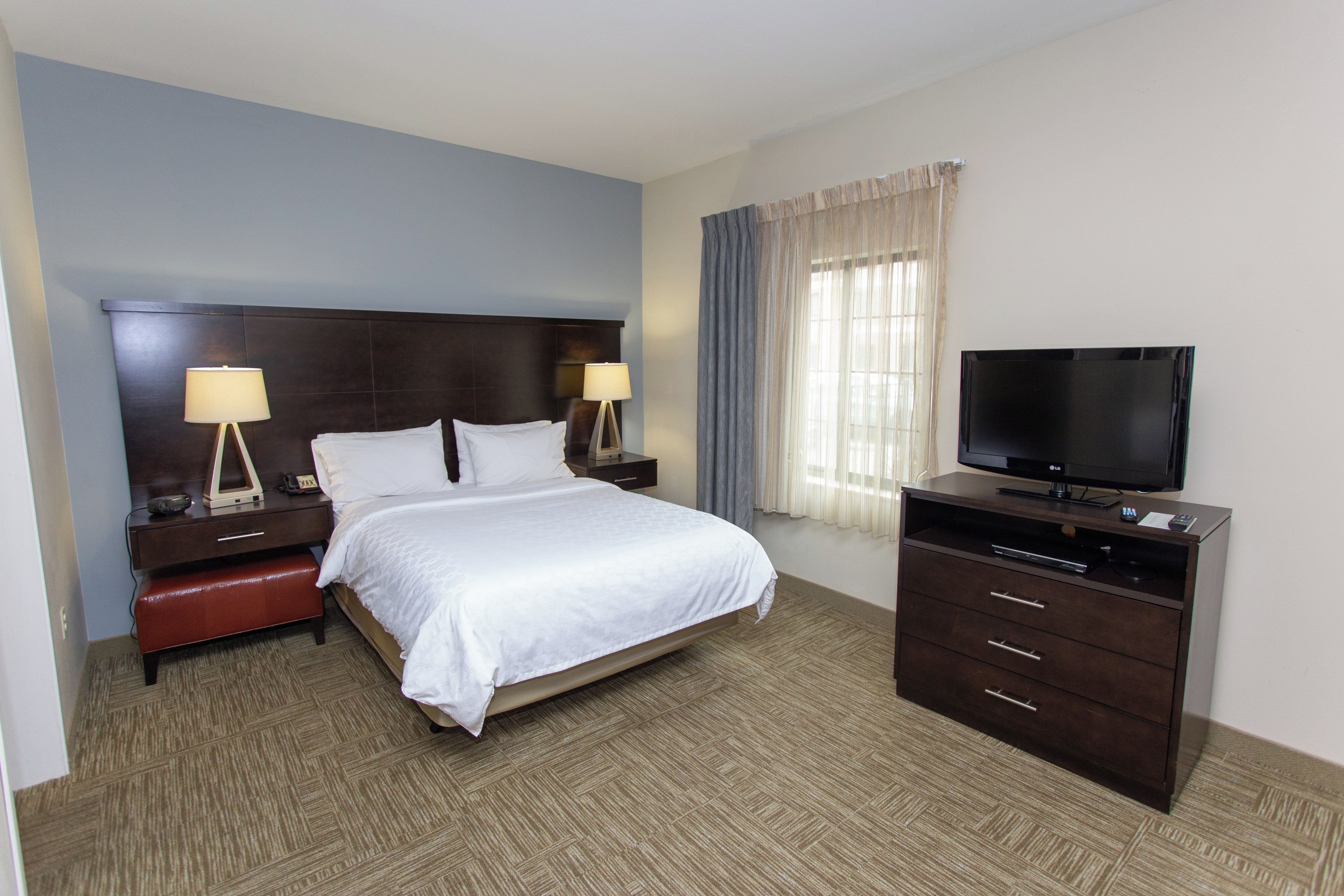 A hotel room with a bed, bedside tables, a TV, and a dresser.