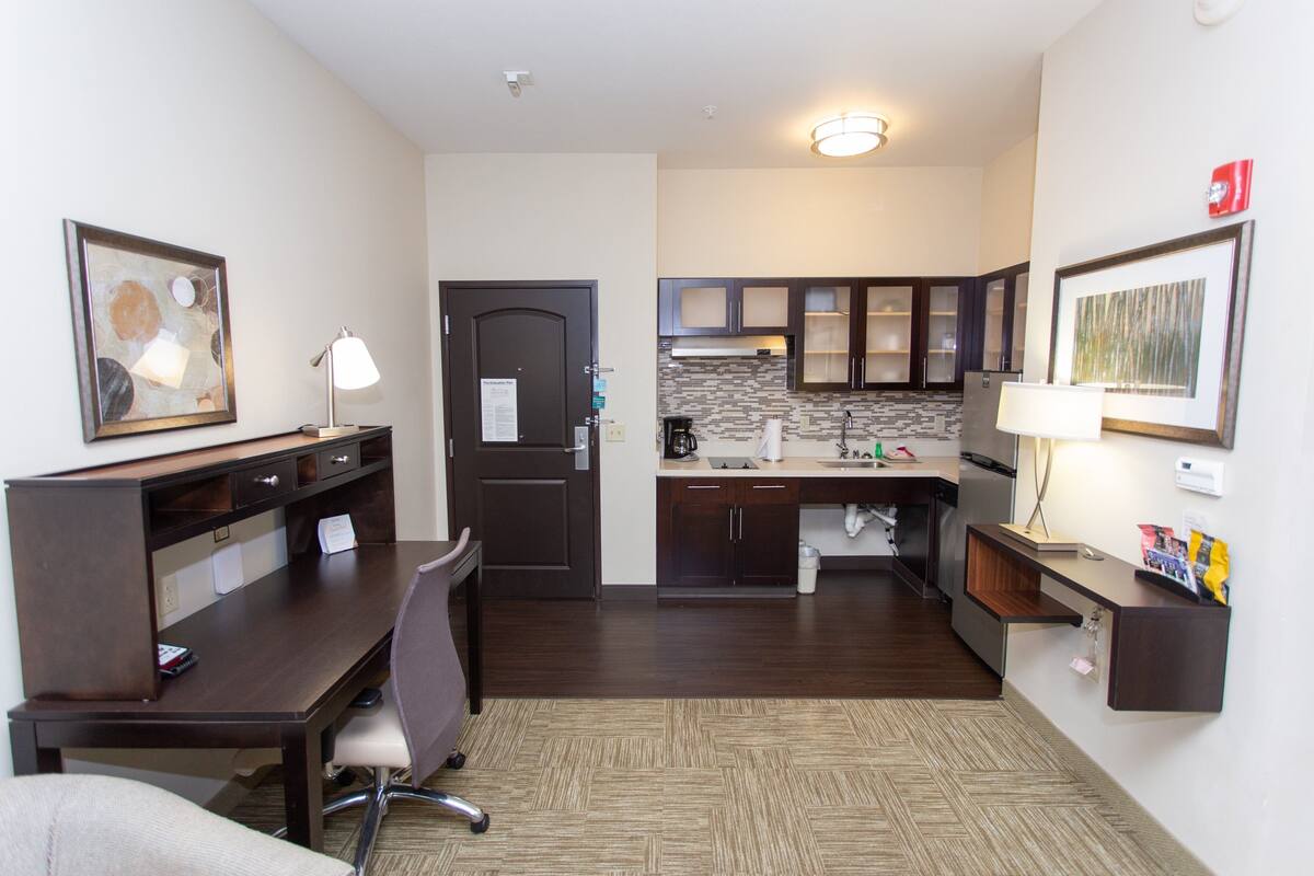 Een hotelkamer met een bureau, stoel, kitchenette en kunstwerken aan de wanden.