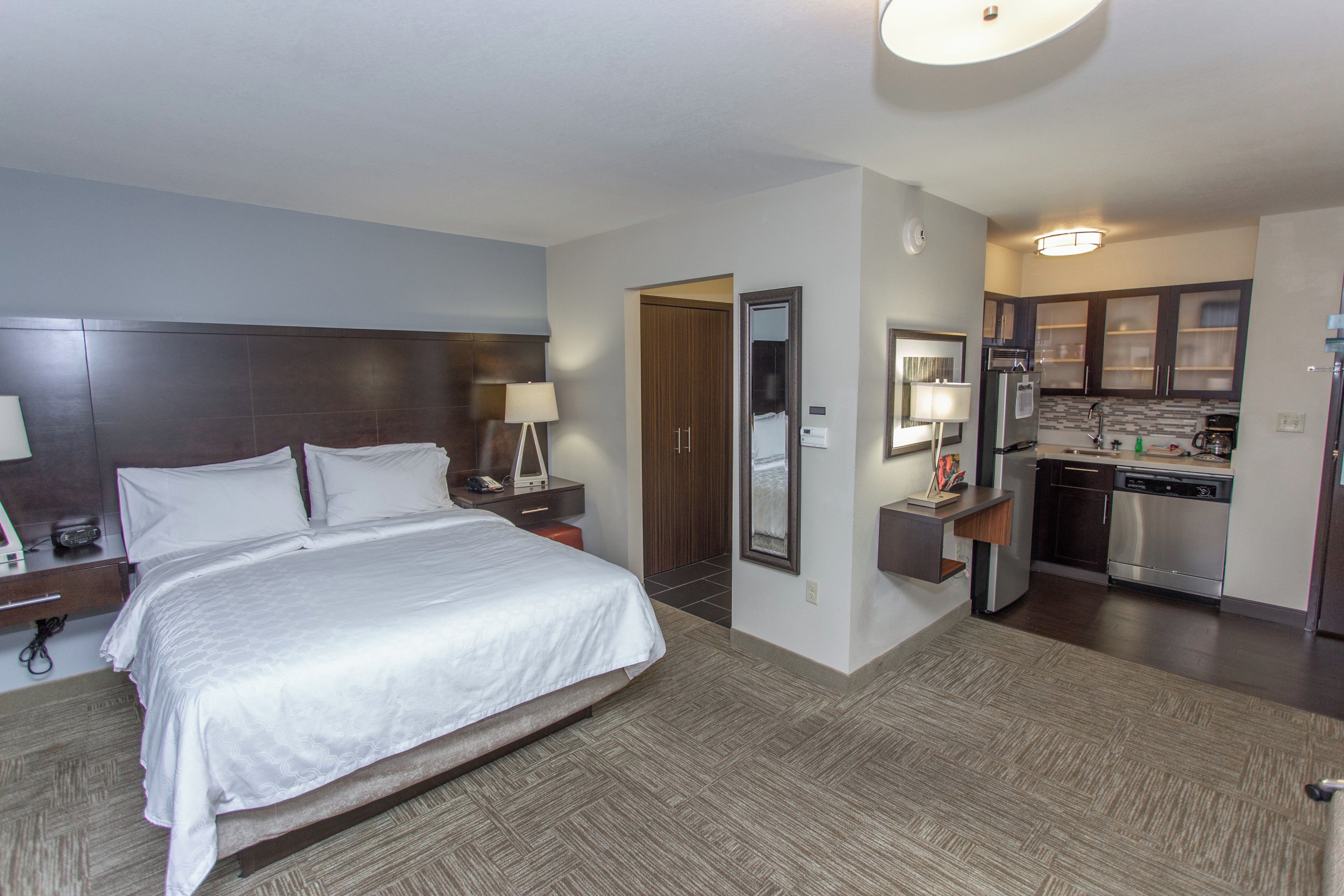 A hotel room with a bed, bedside tables, a mirror, a kitchenette, and a bathroom.