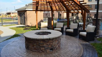 An outdoor patio area with a stone fire pit, wicker chairs, and a wooden pergola.
