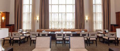 A hotel lobby with a seating area, tables, and large windows with curtains.