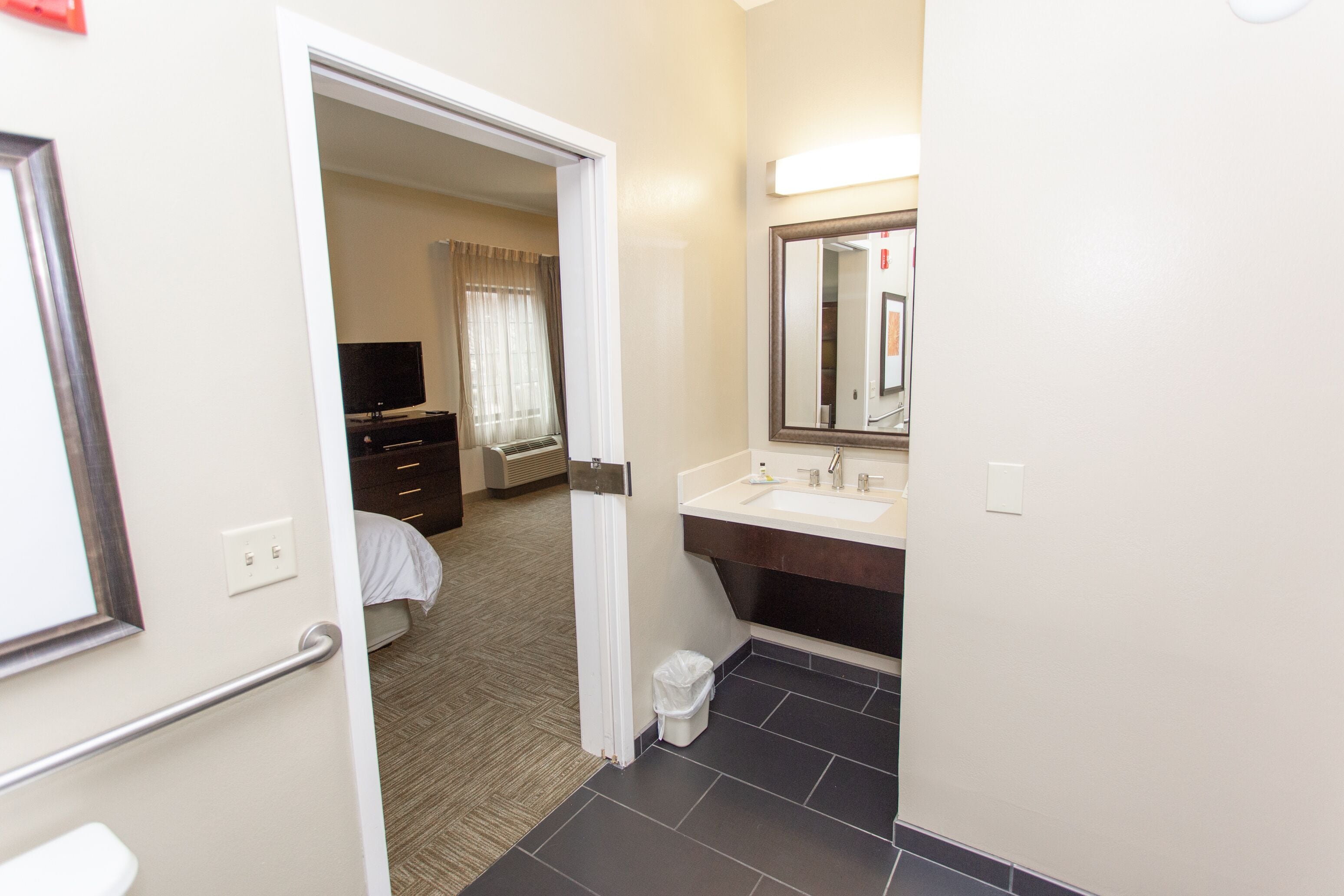 A hotel room with a bed, a dresser, a vanity with a mirror, and a bathroom with a sink and toilet.