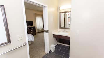 Ein Hotelzimmer mit Bett, Kommode, Schminktisch mit Spiegel und Badezimmer mit Waschbecken und Toilette.