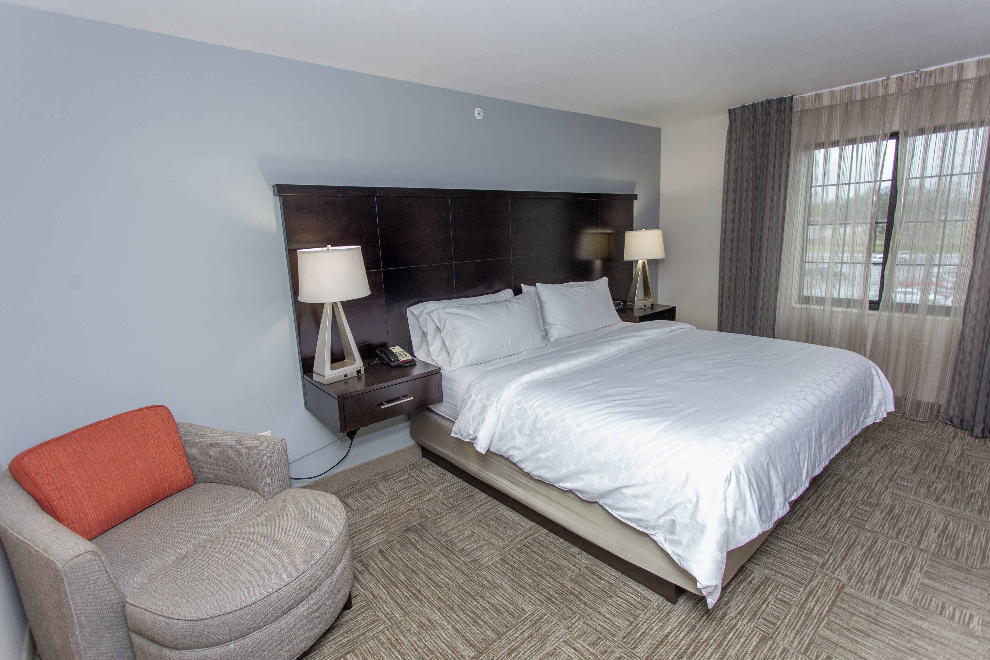 A hotel room with a large bed, two bedside tables with lamps, a chair, and a window with curtains.
