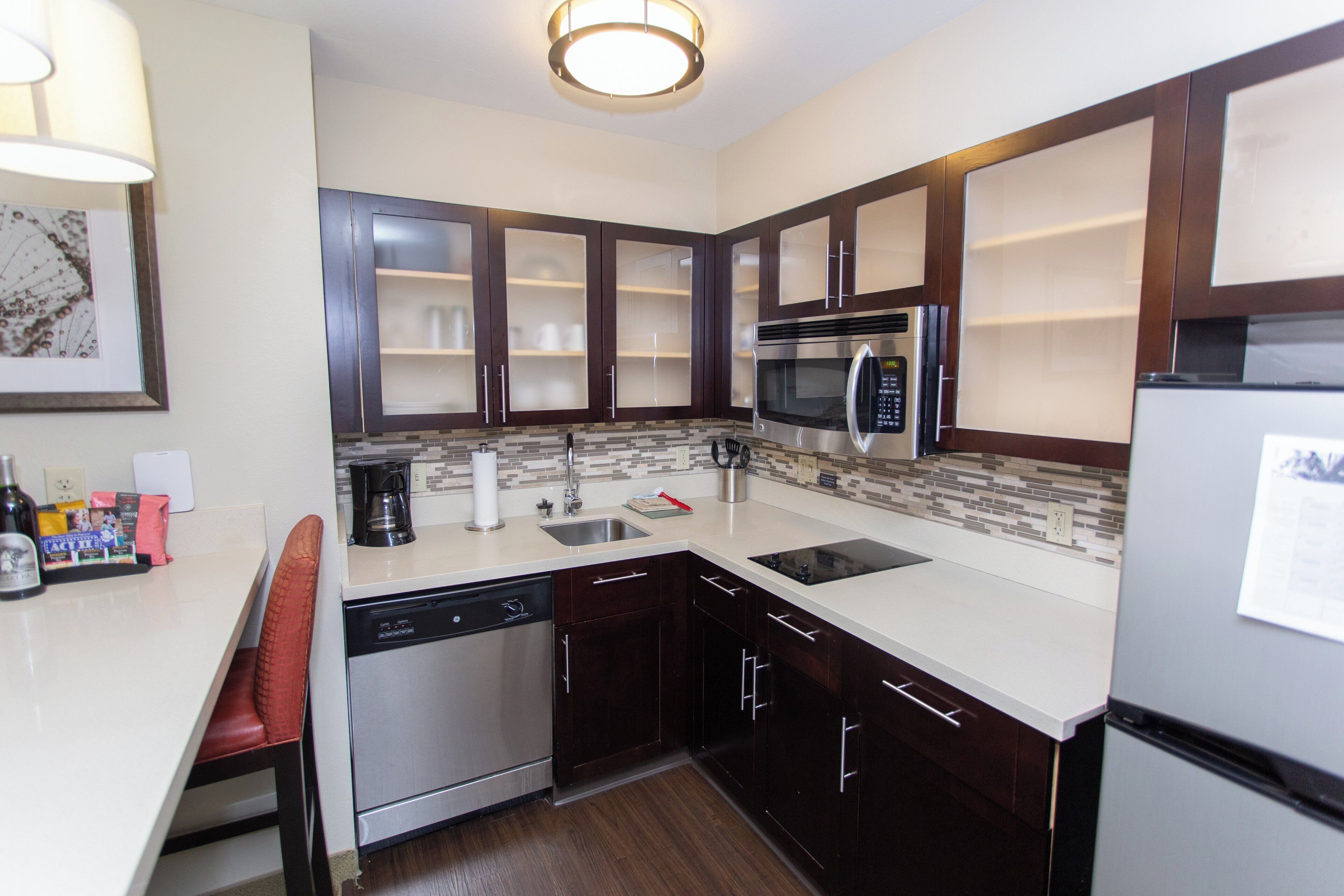 A modern kitchen with dark wood cabinets, a stainless steel dishwasher, a built-in microwave, and a refrigerator.