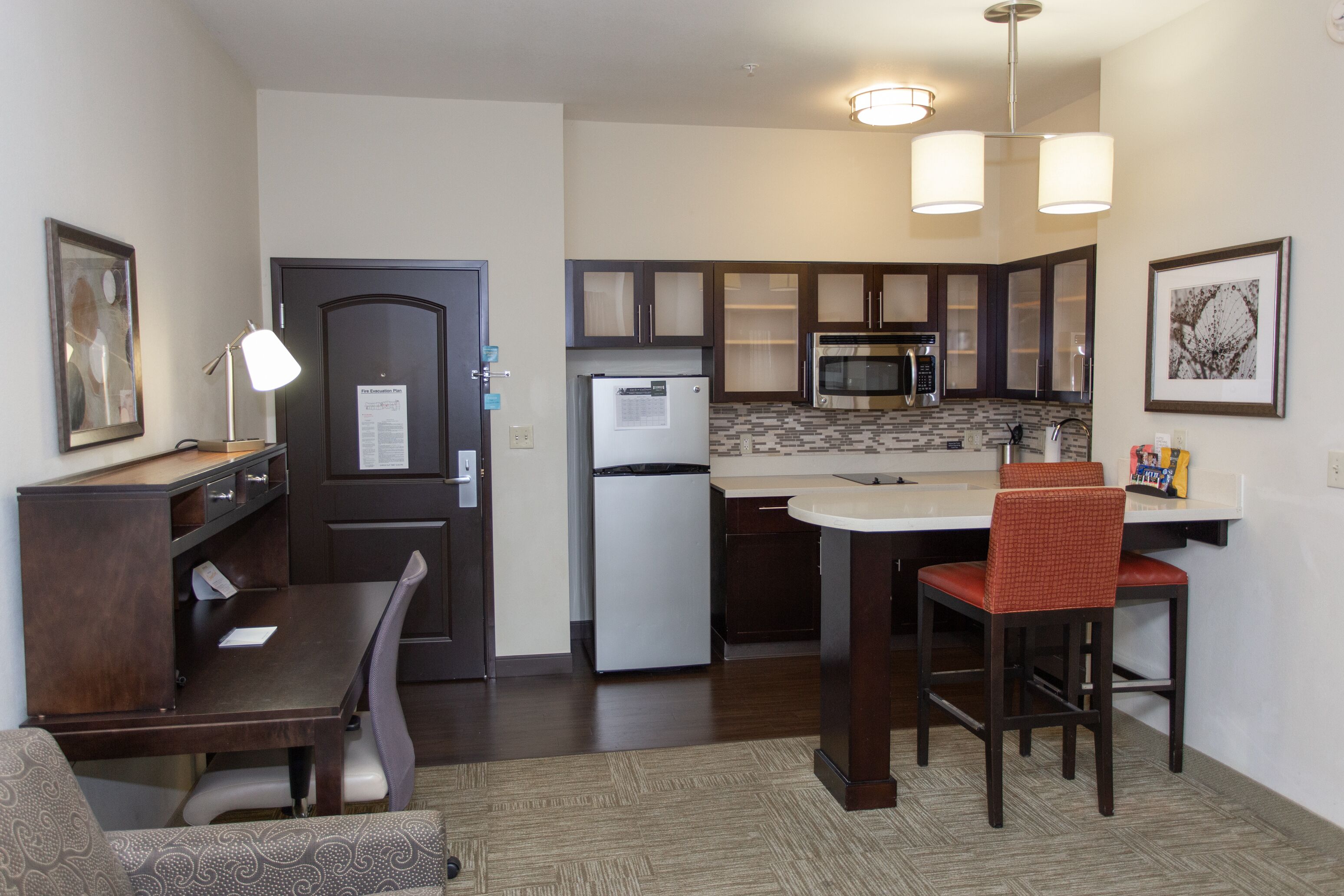 A compact kitchen with dark cabinetry, a refrigerator, a microwave, and a dining area with a chair and table.