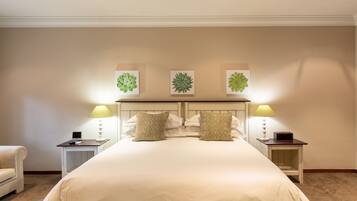 A neatly arranged hotel room with a large bed, two bedside tables with lamps, a chair, and three framed botanical prints on the wall.