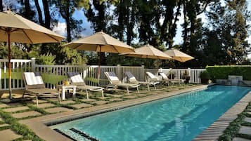 Una piscina al aire libre, sombrillas, sillones reclinables de piscina