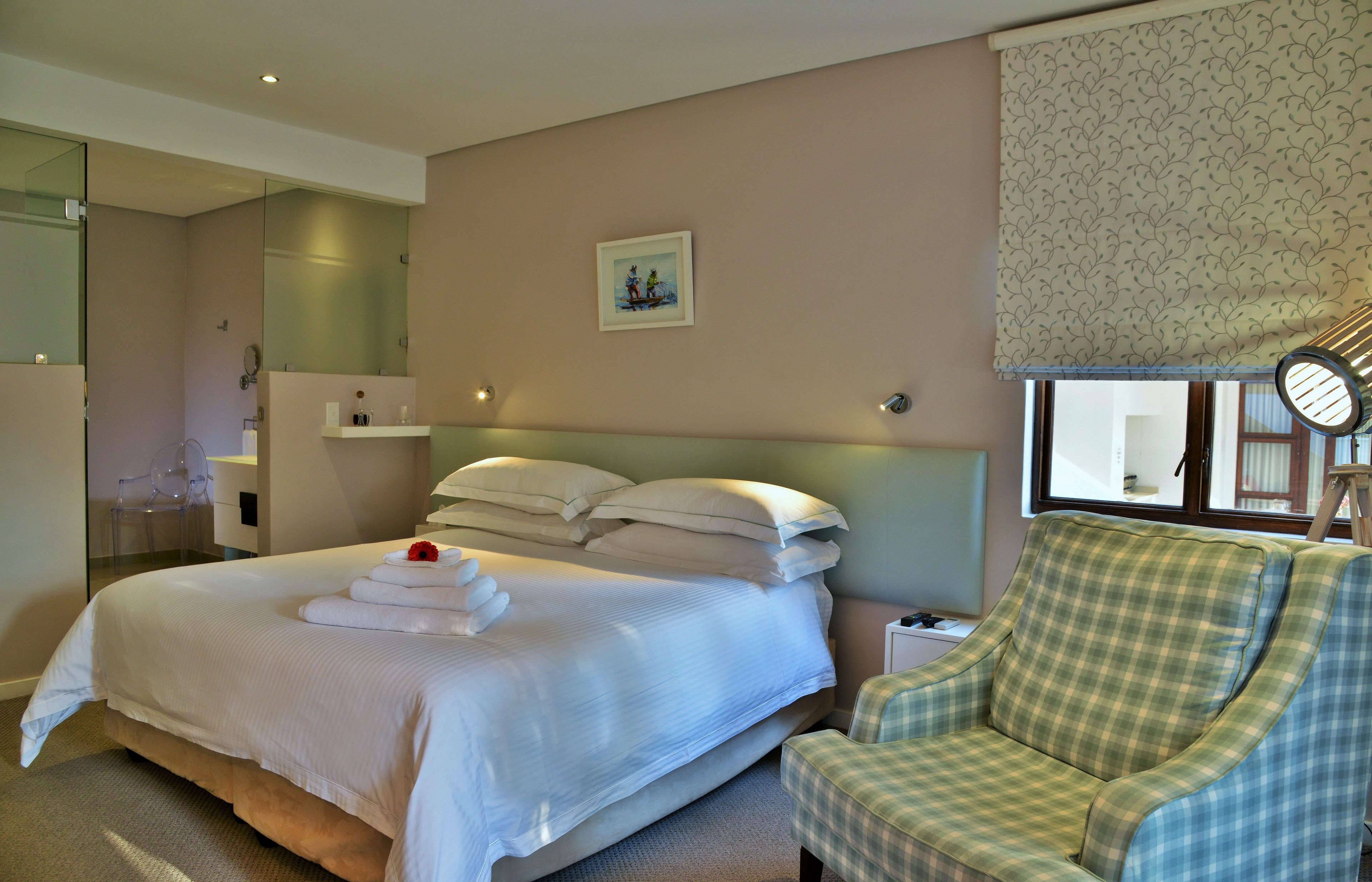 A hotel room with a large bed, a chair, a mirror, a window with a view, and a picture on the wall.