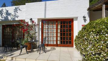 Un edificio blanco con ventanas amplias y una puerta roja, con terraza exterior y un jardín cuidado.