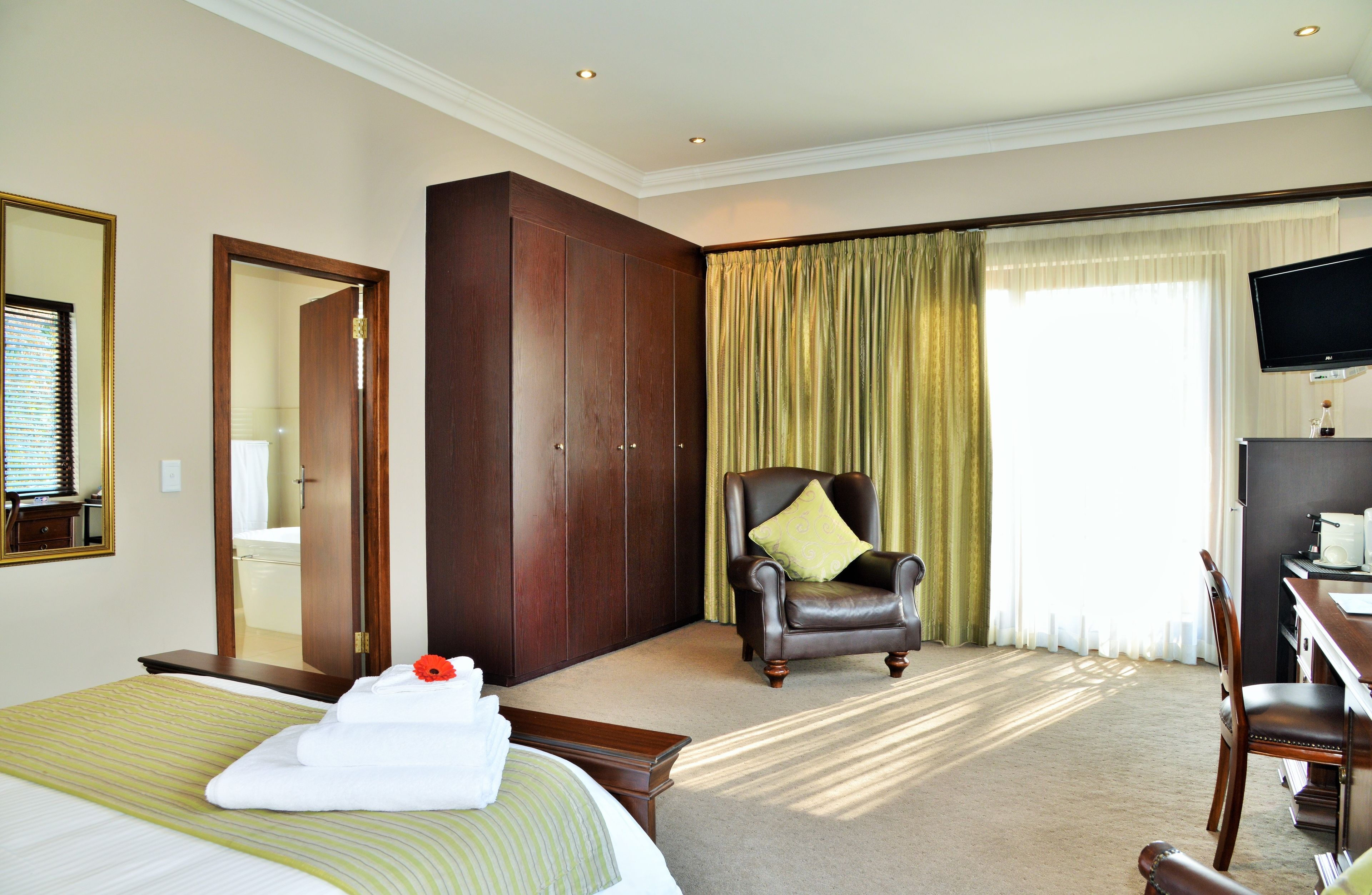 A hotel room with a bed, a chair, a desk, a television, and a wardrobe.