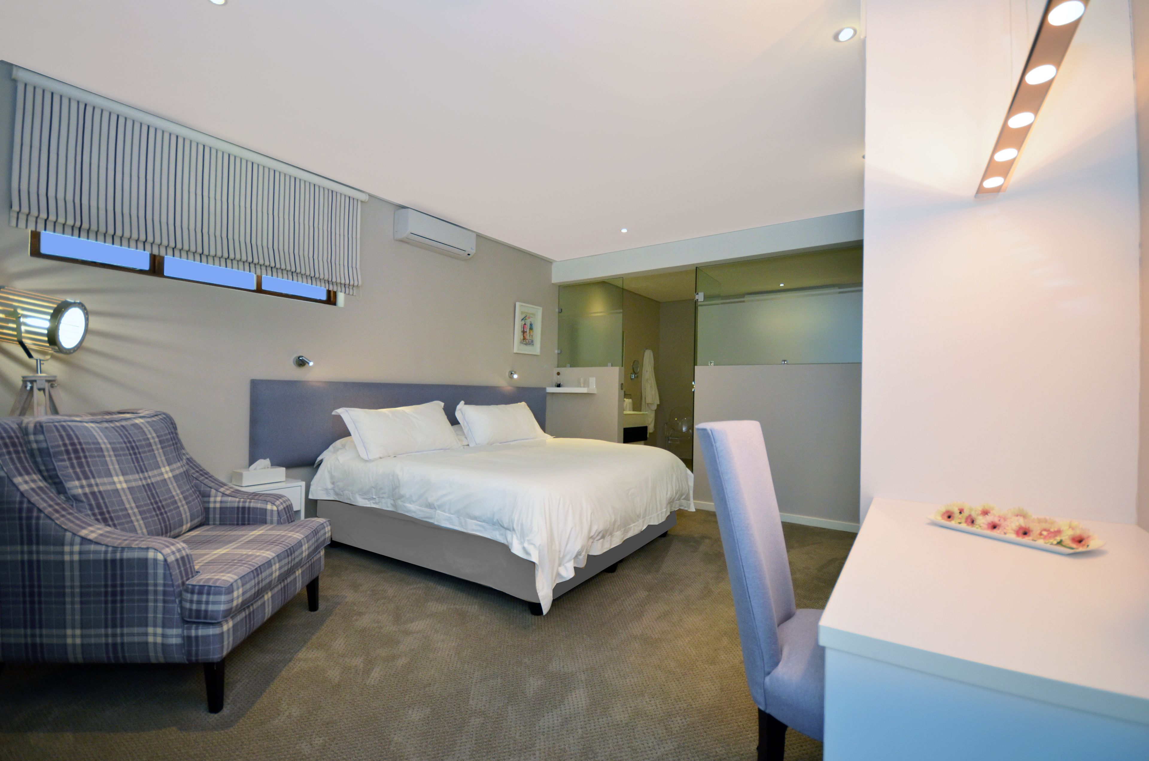 A modern hotel room with a bed, a chair, a small table, and a mirror.