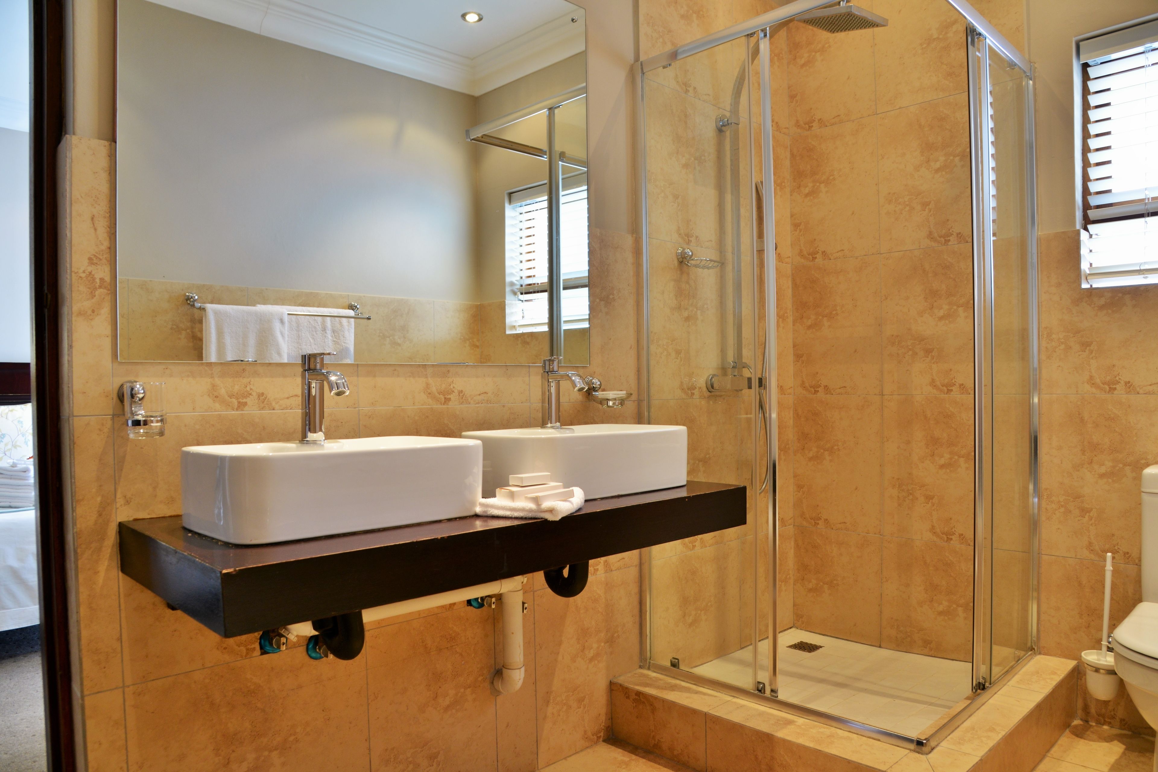 Un baño con un espejo grande, dos lavamanos, cabina de ducha y un inodoro.