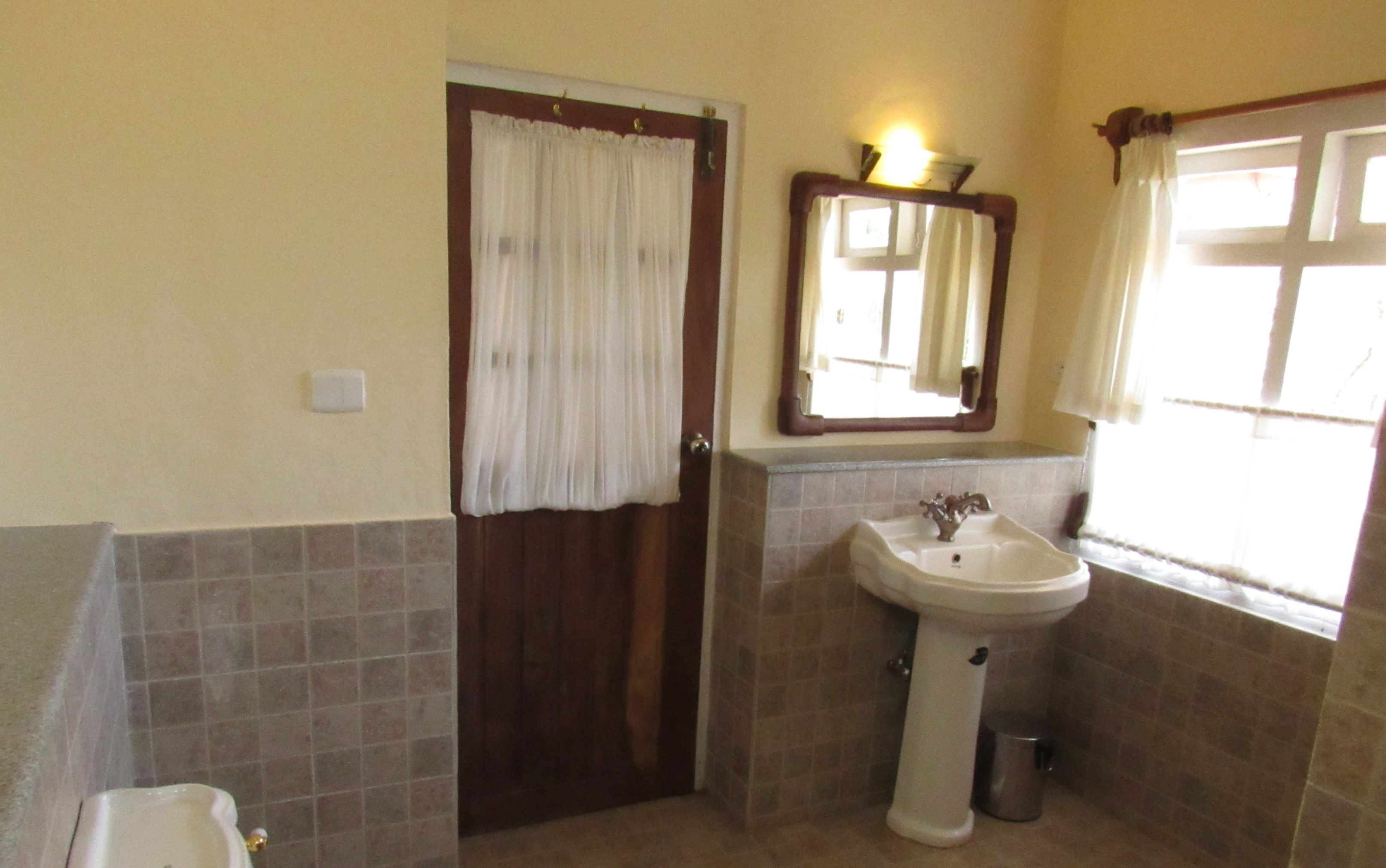 Une salle de bain avec un lavabo, un miroir et une porte avec un rideau.