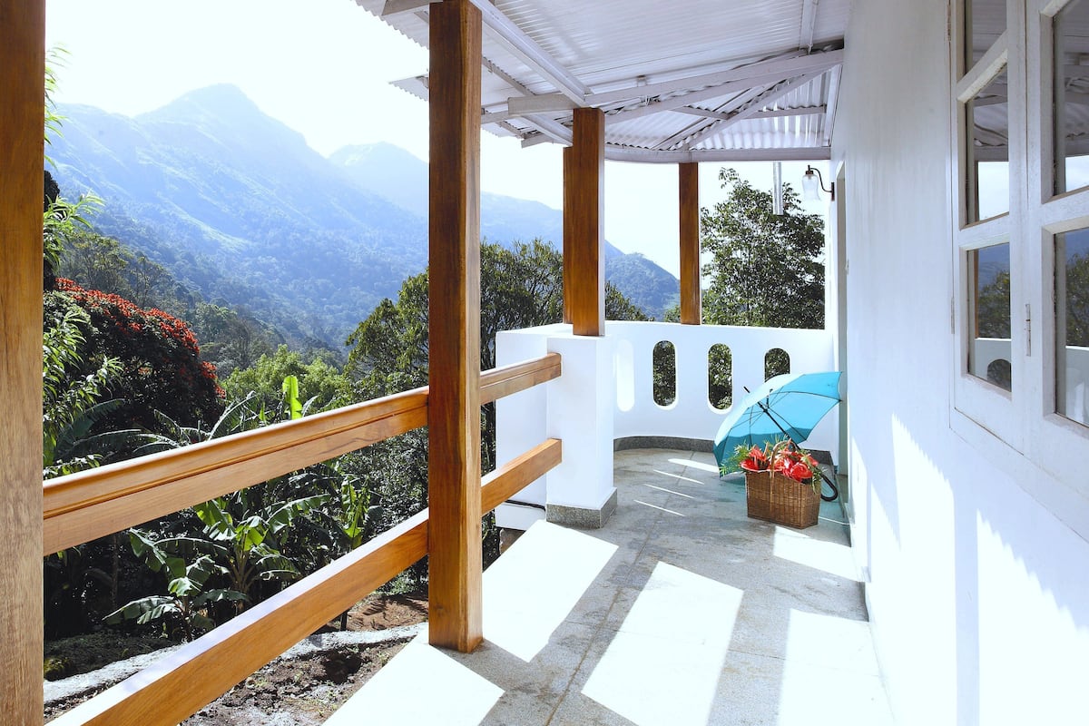 Un balcone coperto con vista sulle montagne, ringhiere in legno e un cesto di fiori.