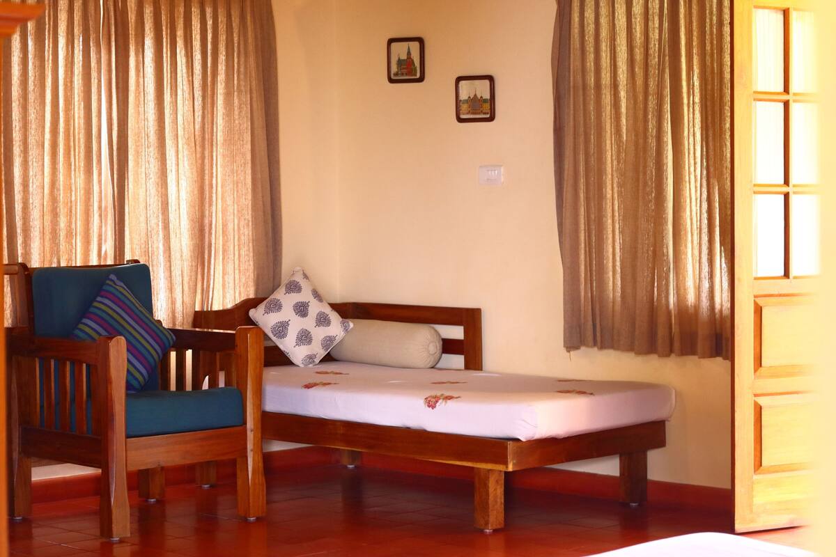 Un letto singolo con struttura in legno, una sedia blu con cuscino a righe e due quadri appesi al muro.