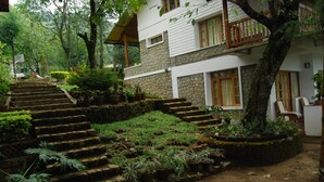 A two-story stone building with a staircase leading to a wooden balcony. - Windermere Estate (Devikolam)