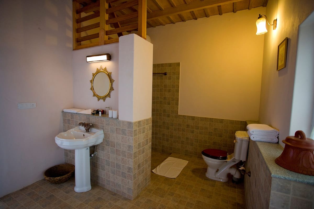 Un bagno con un lavandino su piedistallo, un water, zona doccia e uno specchio con cornice decorativa.