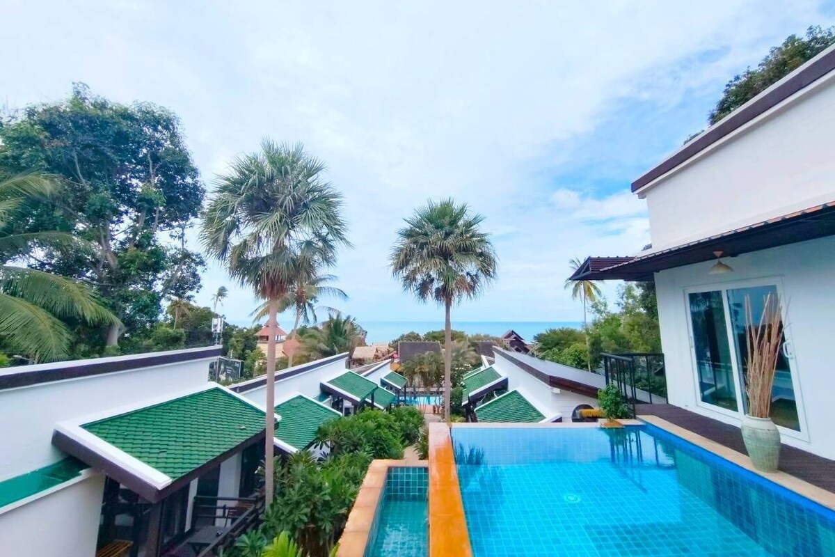 A resort with a swimming pool, palm trees, and a view of the ocean.