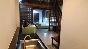 A narrow kitchen with a sink, a green appliance, and a wooden chair. A bed with a green pillow is visible through a doorway in the background. - Sasitara Residence (Koh Samui)