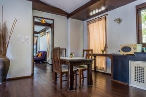 A dining area with wooden chairs and a table, a microwave on the counter, and a window with curtains. - Sasitara Residence (Koh Samui)