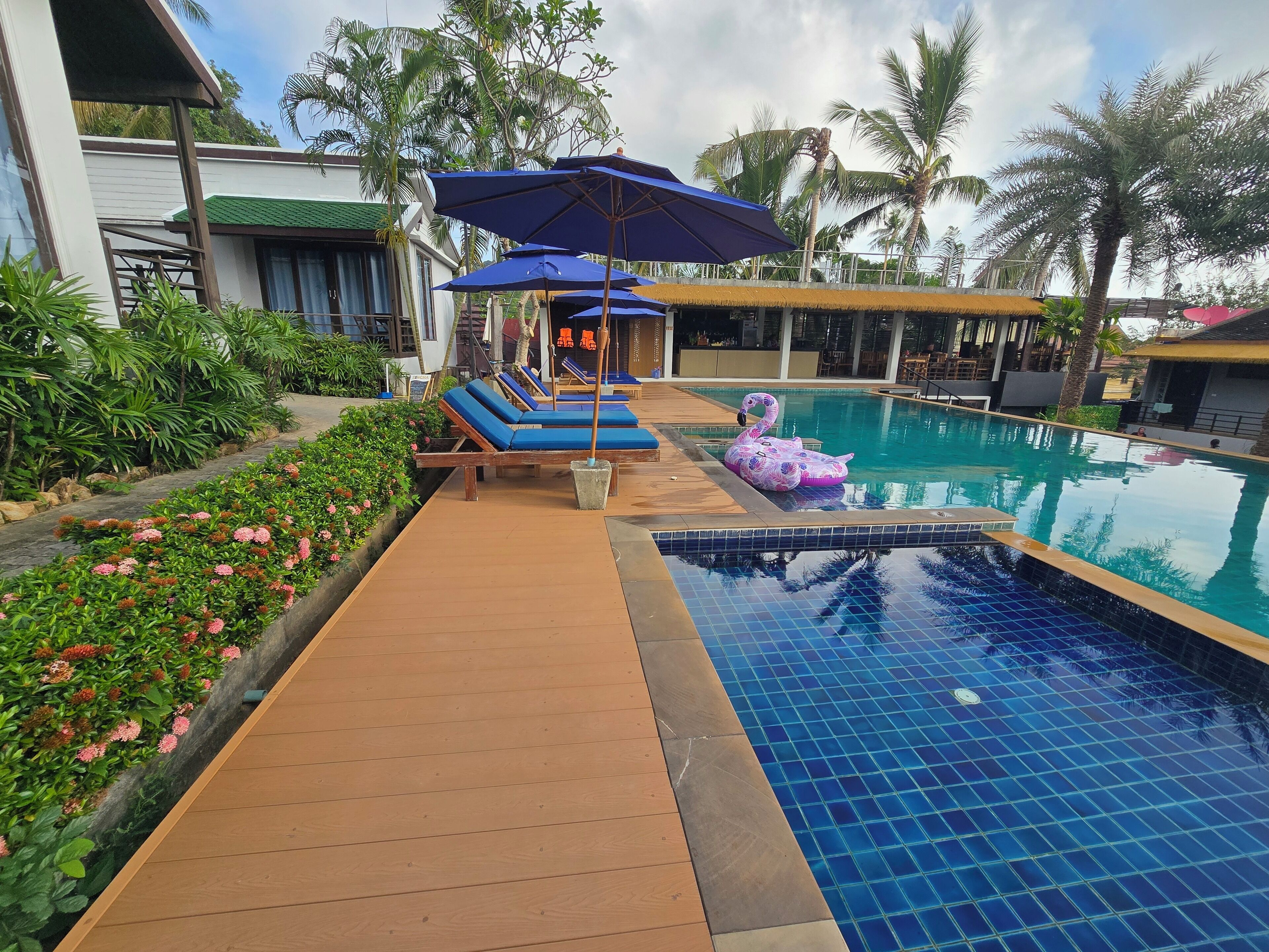 Zona de piscina con sillones de descanso, un flotador con forma de flamenco y un jardín tropical.