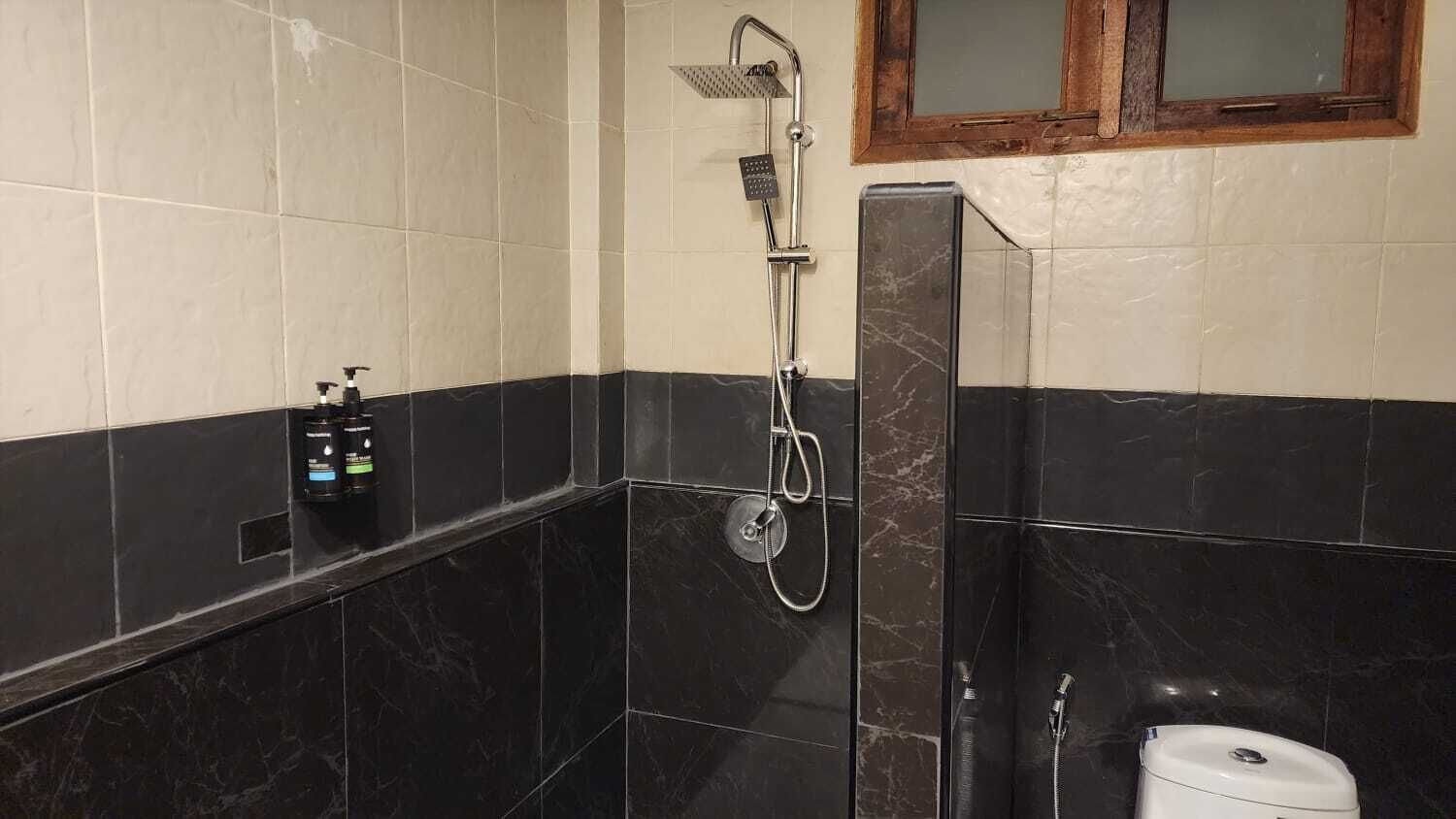 Un baño con ducha, inodoro y un estante con artículos de aseo.