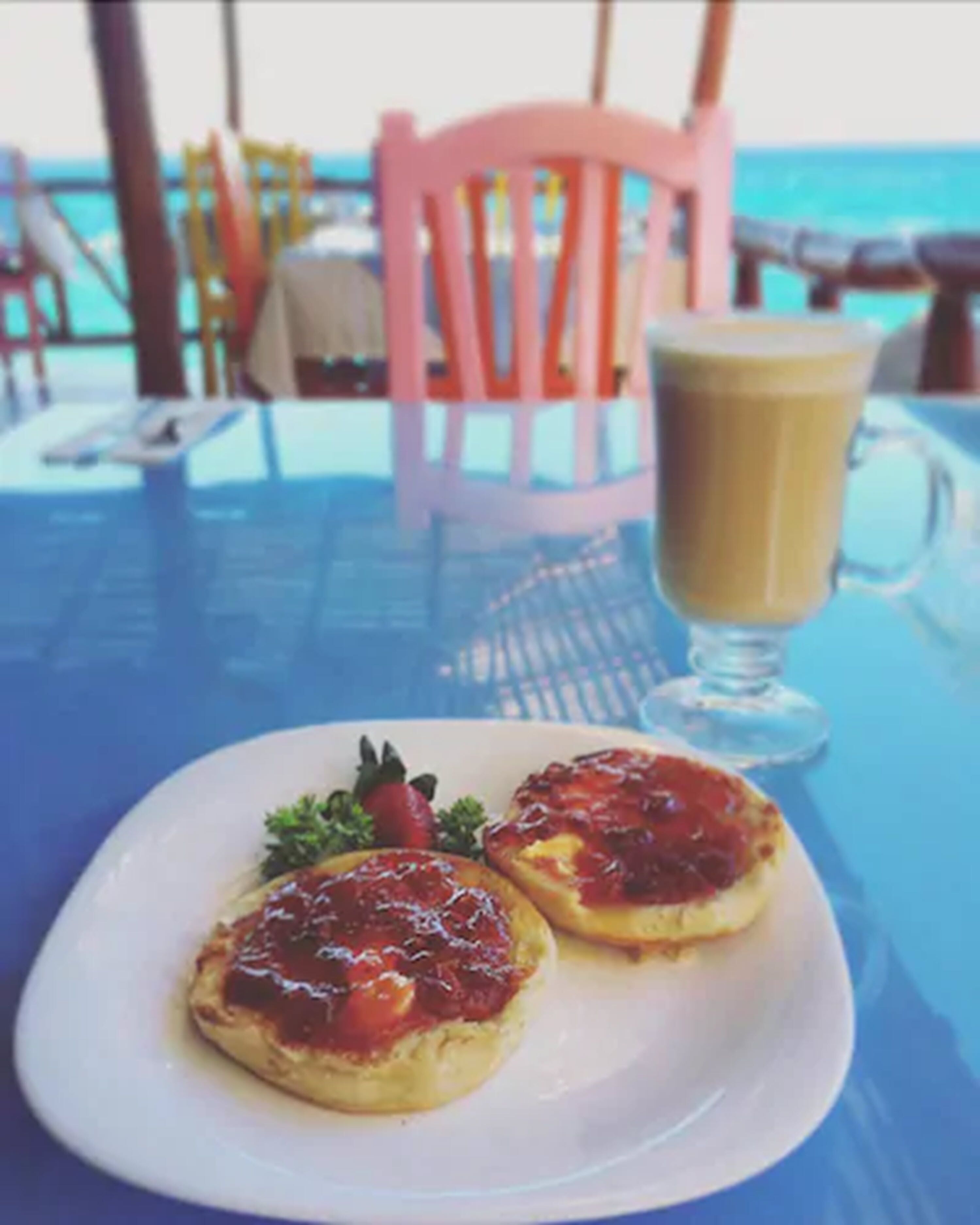 A table with a plate of food and a glass of beverage, set against a view of the ocean.