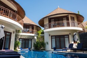 Un resort con piscina, sillas de descanso y un edificio de dos pisos con balcón.