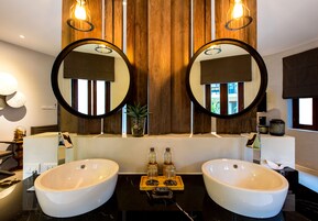 Un baño con dos lavamanos grandes y blancos, paneles de madera y dos espejos redondos.