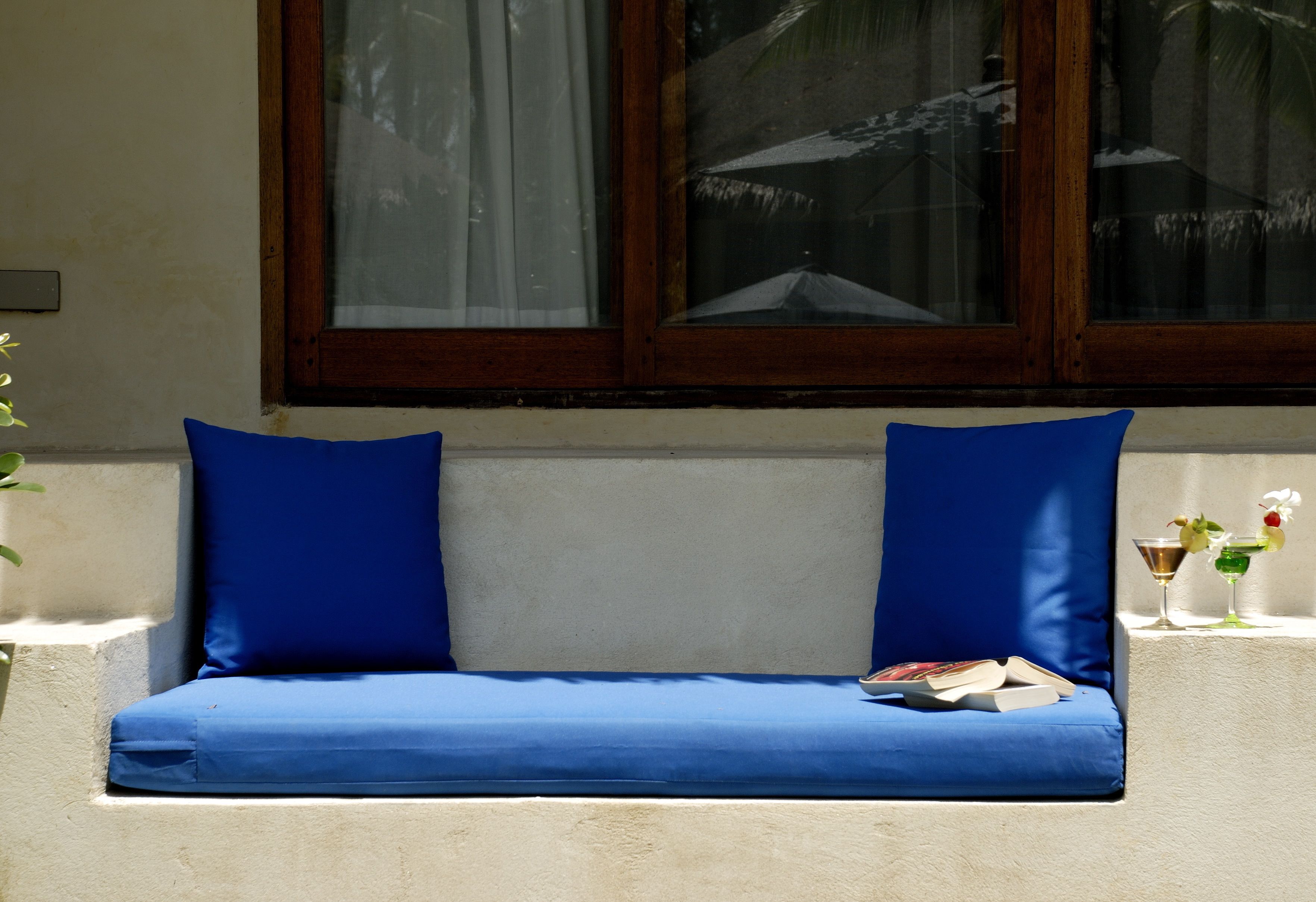 A blue cushioned bench with a book and two drinks against a wall.