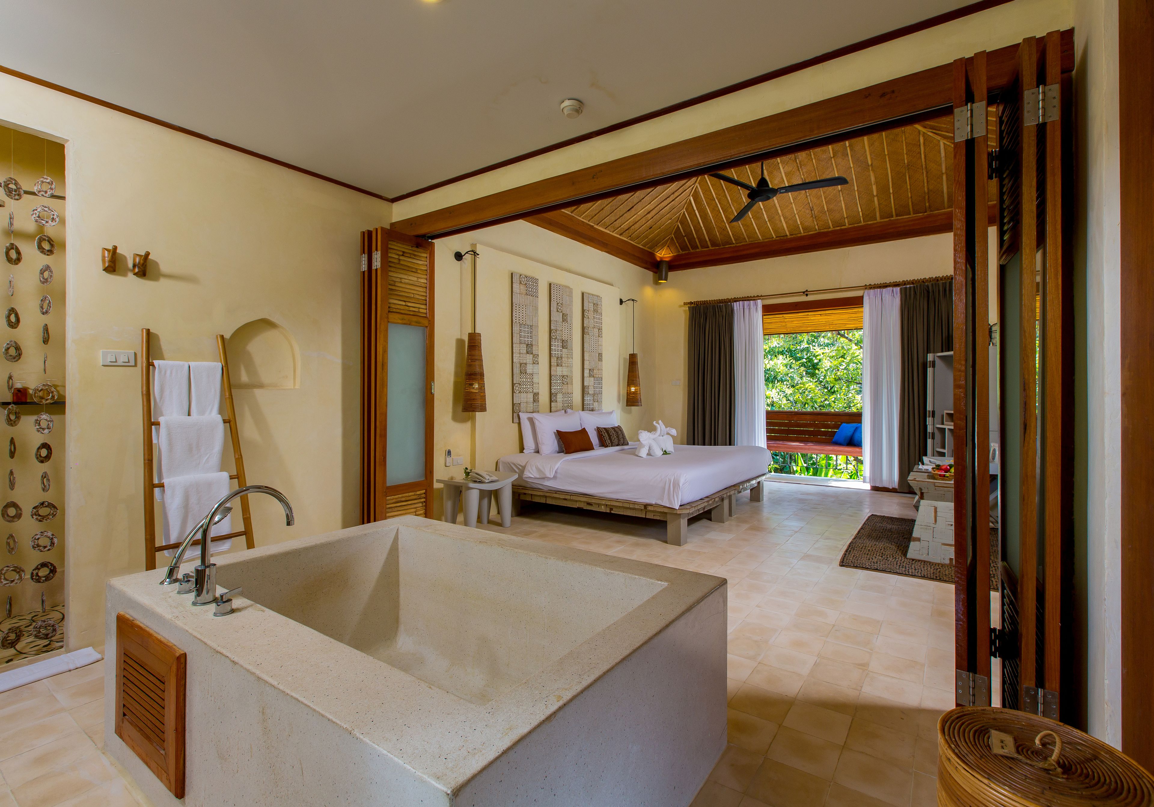 Une chambre spacieuse avec une grande baignoire, un lit avec des oreillers et une vue sur l’extérieur.
