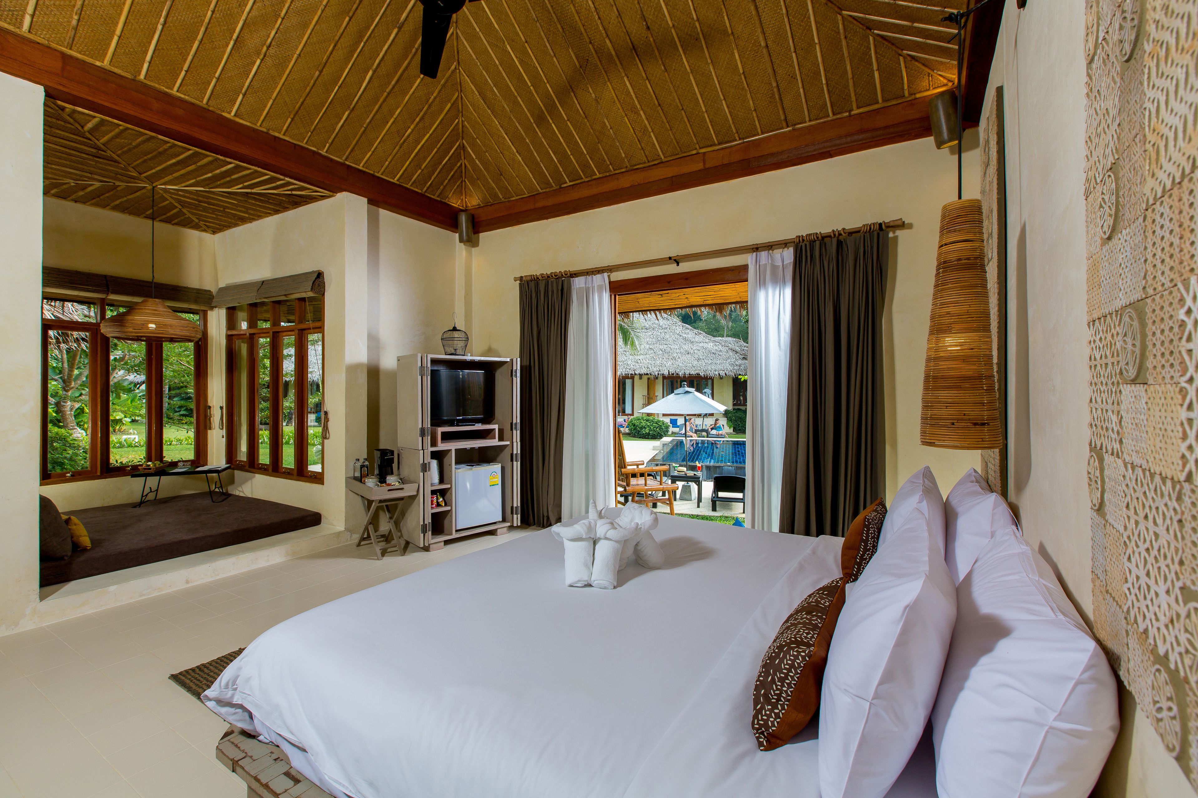 A hotel room with a large bed, a television, a small table, and a view of an outdoor pool area.