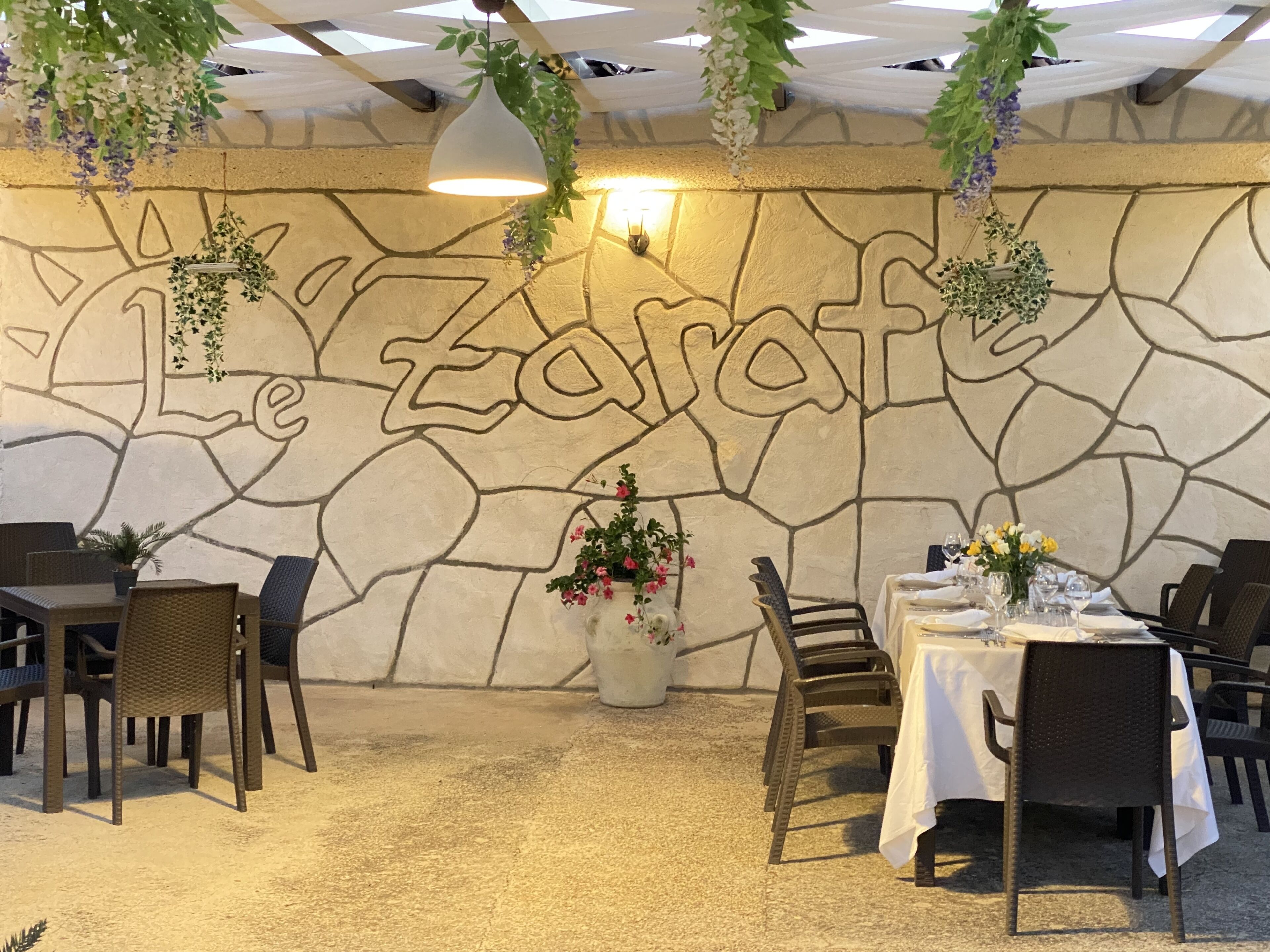Interior de restaurante con pared de piedra, plantas colgantes y mesas dispuestas para comer.