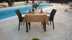 A table set for two with a bottle of champagne, a vase of flowers, and a candle on a patio by a pool. - Le Zarafe (Caltabellotta)
