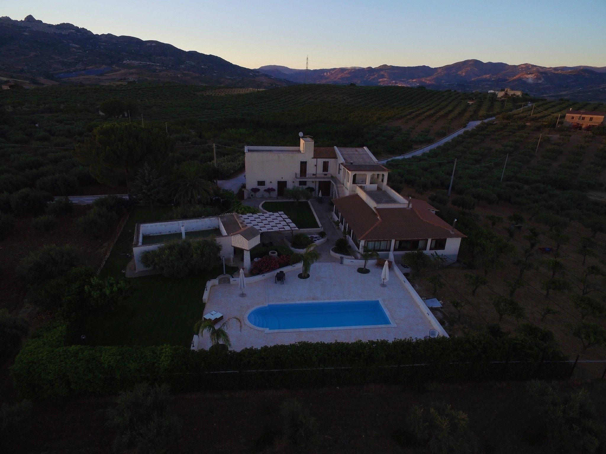 A large house with a swimming pool, surrounded by a vineyard and mountains in the background.