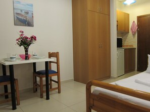 A room with a bed, a dining table with chairs, a small kitchenette, and a wooden wardrobe. - The Sea-View Apartments (Rethymno)