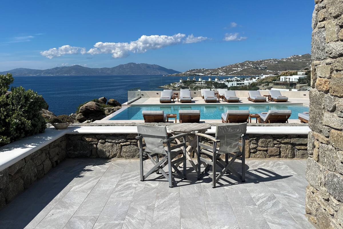 A pool area with lounge chairs and a view of the sea and mountains.