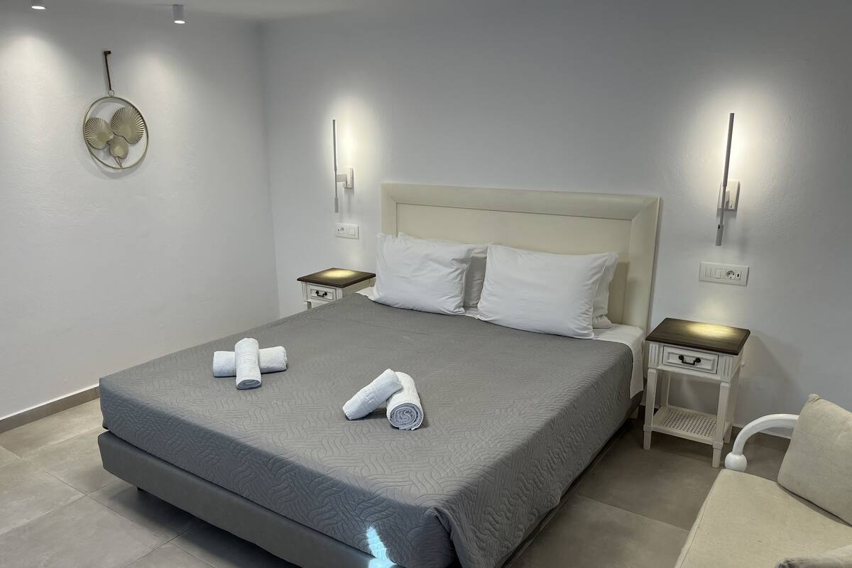A neatly made bed with two rolled towels, a white headboard, and two bedside tables with lamps.