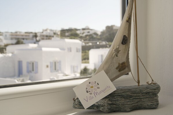 A sailboat model with a card labeled "Villa Margarita" on a rustic base, positioned by a window overlooking a coastal town.
