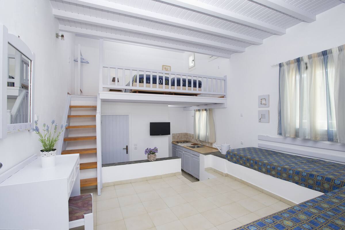 A compact, well-lit room with a bunk bed, kitchenette, and a small seating area.
