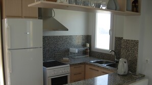 A compact kitchen with a refrigerator, stove, sink, and a kettle. - King's View (Lesvos)