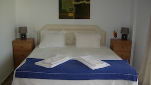 A neatly made bed with a blue and white bedspread, two white pillows, and two bedside tables with lamps and a small decorative item. - King's View (Lesvos)