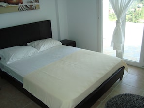 Cama bem arrumada com lençóis brancos, cabeceira escura e uma pequena mesa de cabeceira.