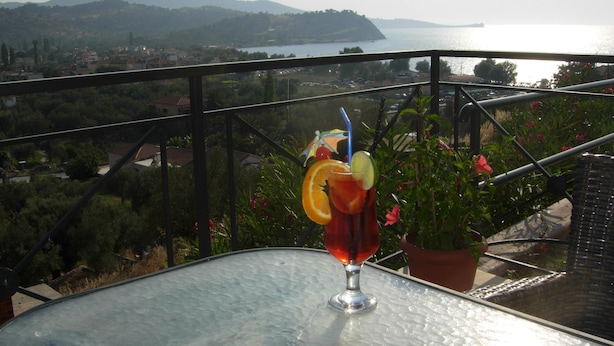A balcony with a table, a potted plant, and a glass of drink with fruit garnish. - King's View (Lesvos)