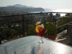 A balcony with a table, a potted plant, and a glass of drink with fruit garnish.